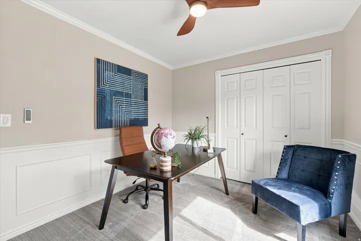 Carpeted room featuring wainscoting, crown molding, and a ceiling fan