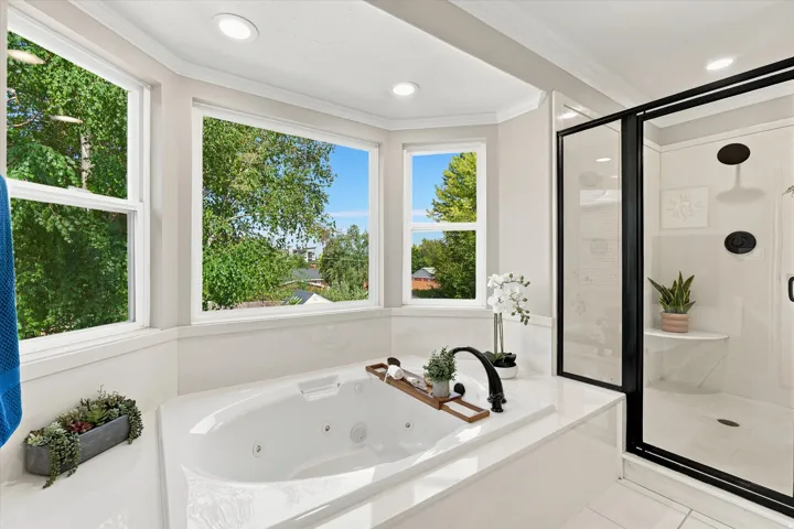 Bathroom featuring a built-in jetted tub, expansive window array, and an enclosed shower with matte black fixtures and a built-in bench