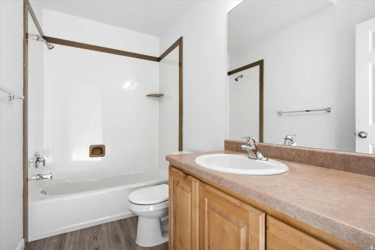 Bathroom featuring a white bathtub and shower combination with a single shelf, wood-finish flooring, light wood vanity with an integrated sink, and a large wall-mounted mirror