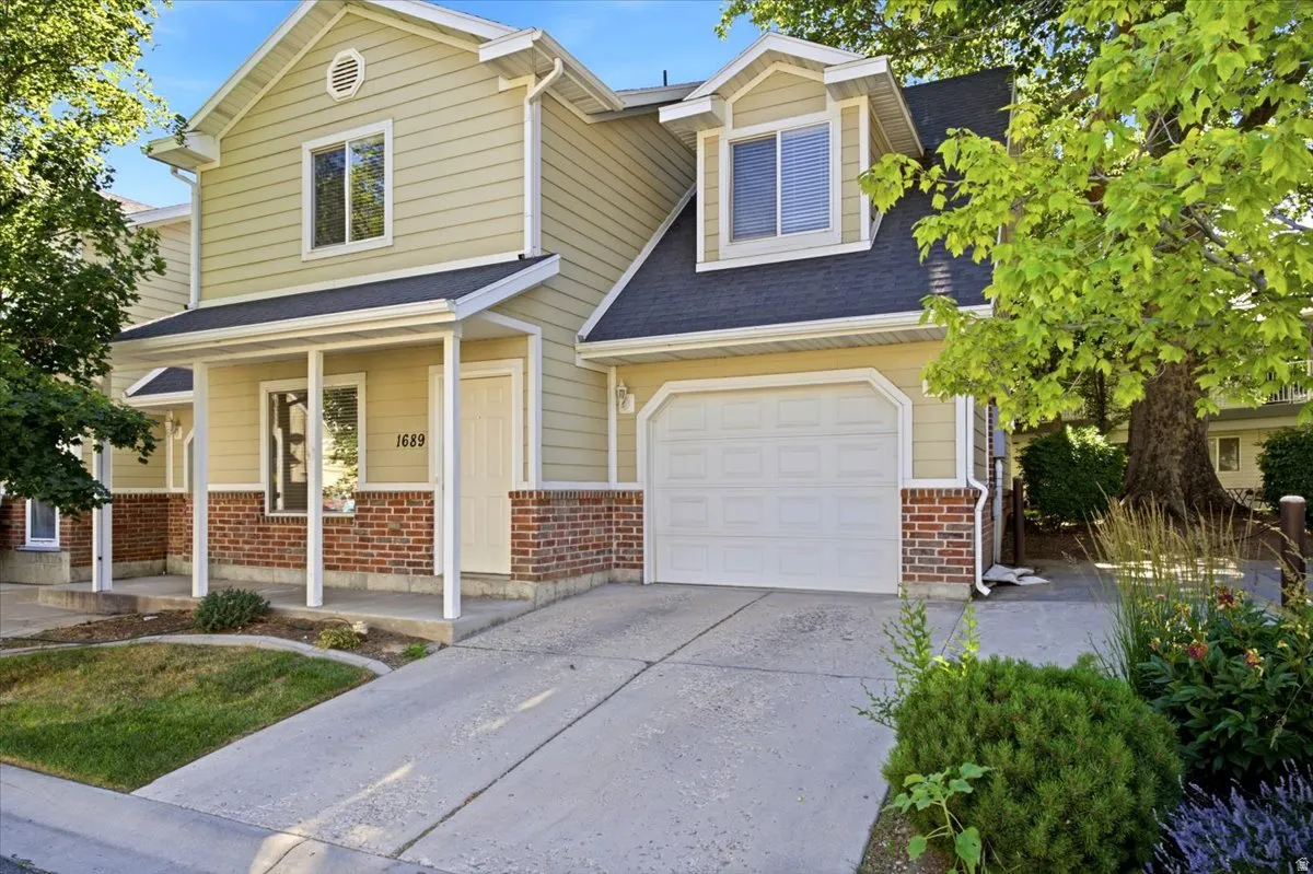 Light-colored siding exterior featuring a covered porch with white columns, red brick accents, an attached garage, and a concrete driveway