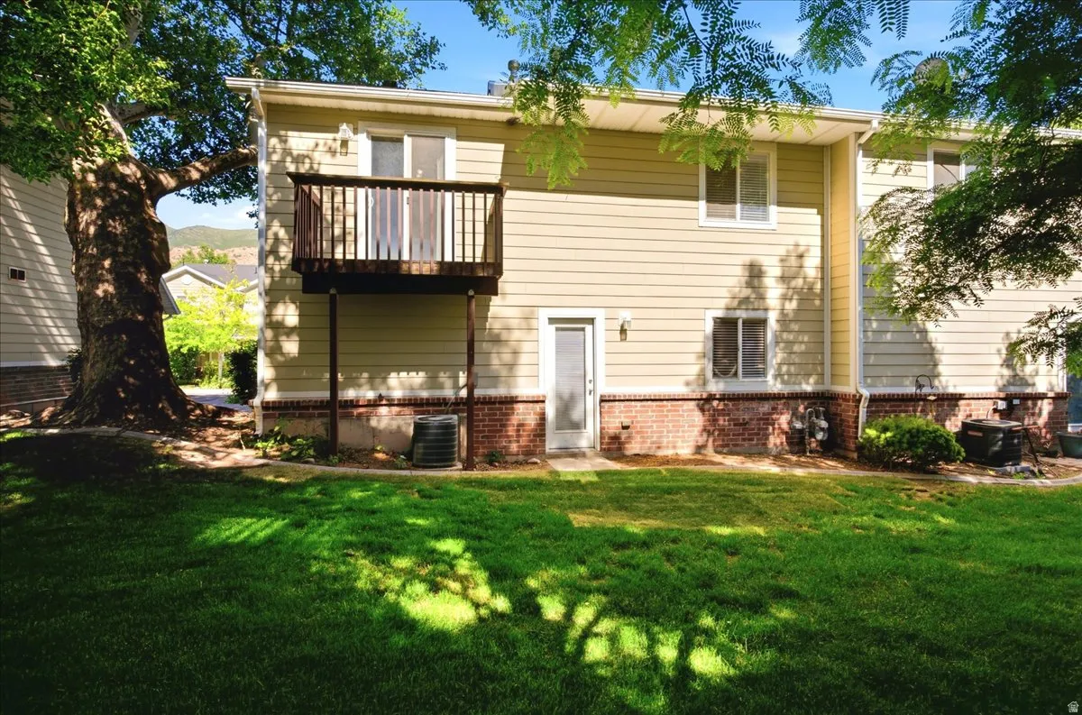 Expansive grassy lawn with a large mature tree, a ground-level exterior door, and a second-story wooden deck
