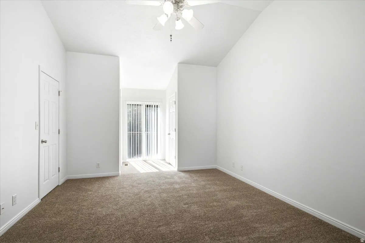Carpeted room featuring a ceiling fan, vaulted ceiling, white baseboards, and a glass sliding door with vertical blinds