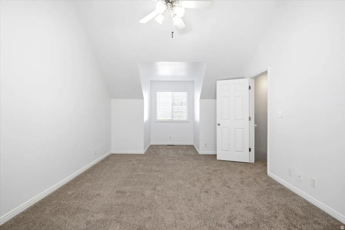 Carpeted room featuring a ceiling fan, sloped ceilings, and a window with blinds