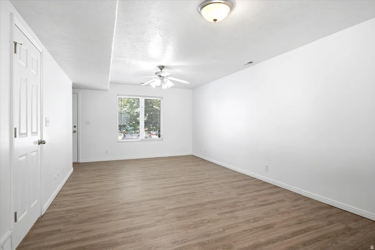 Spacious room featuring wood-finish flooring, white walls, and a ceiling fan with integrated lighting