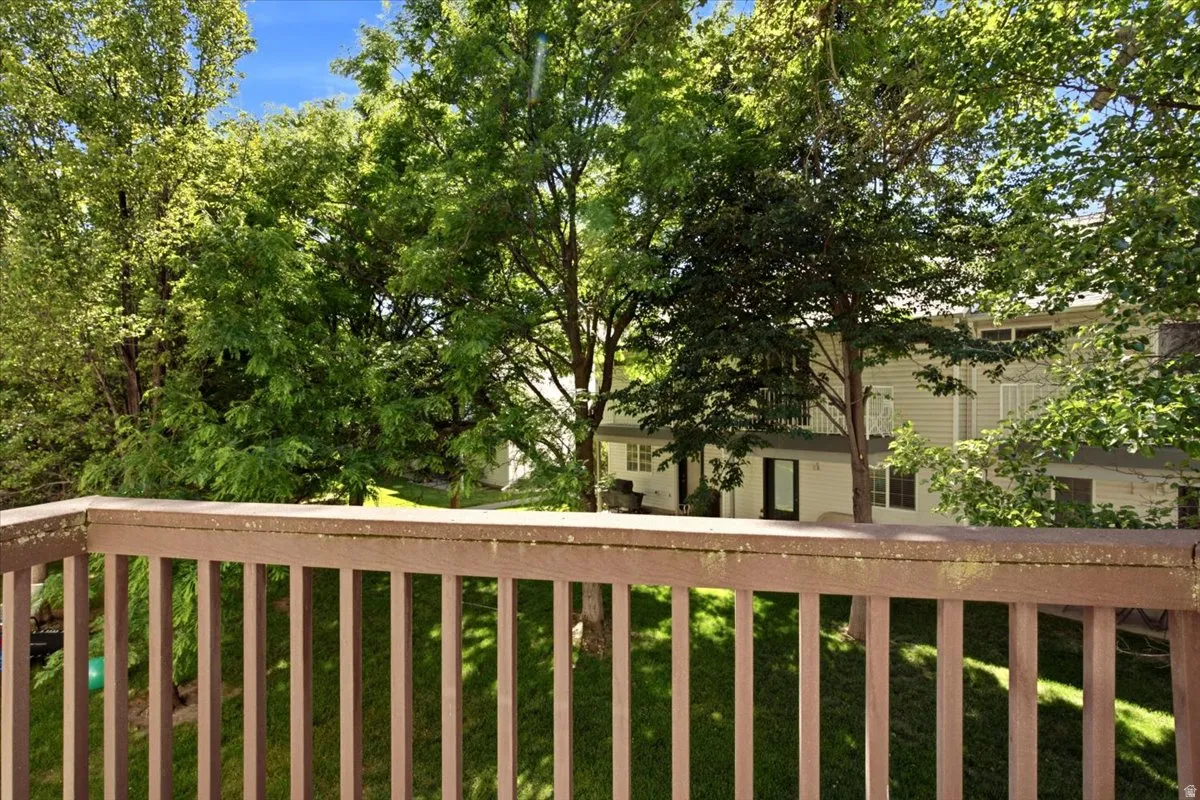 Deck railing framing a verdant, treed landscape with a multi-level structure featuring siding and glass doors