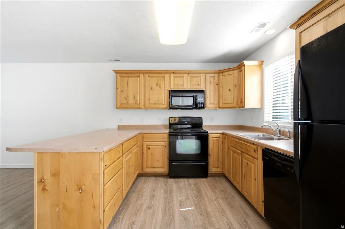 U-shaped kitchen featuring wood cabinetry, laminate countertops, wood-finish flooring, and black appliances