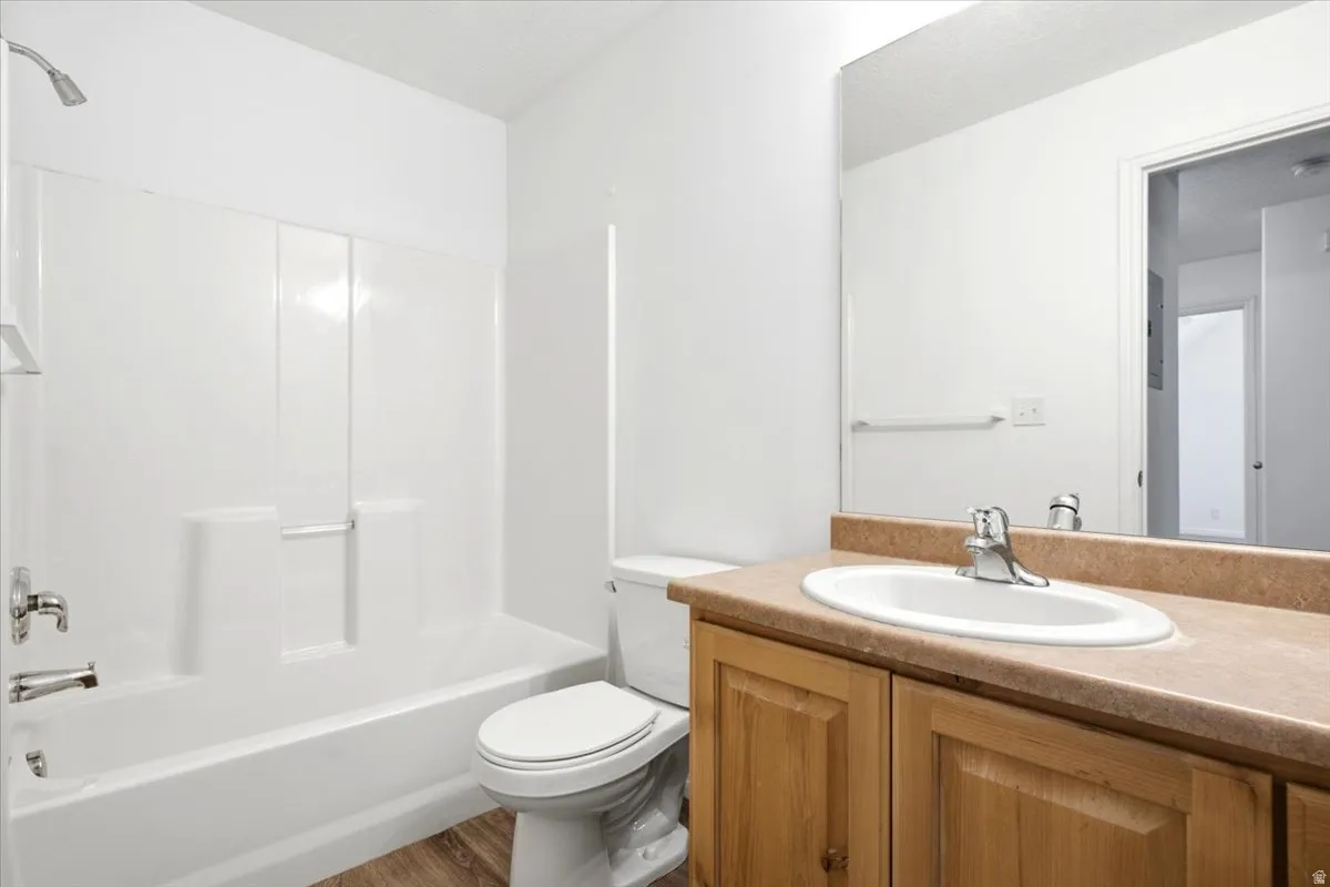 Full bathroom featuring a white tub and shower combination with chrome fixtures, a wood-finish vanity with a built-in sink, a neutral countertop, and wood-finish flooring