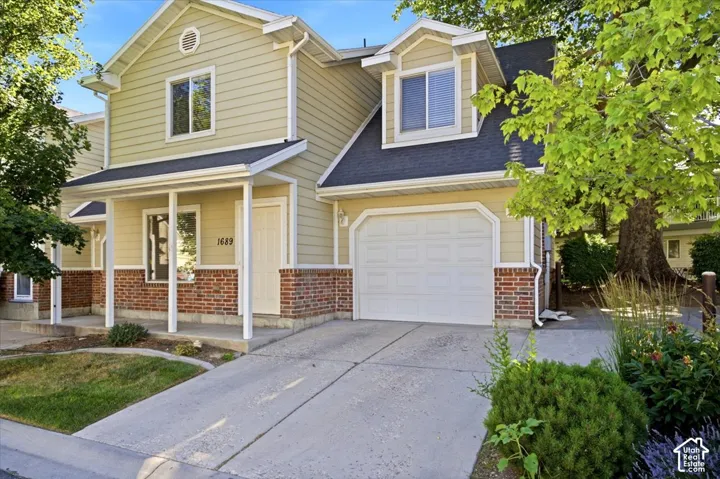 Light-colored siding exterior featuring a covered porch with white columns, red brick accents, an attached garage, and a concrete driveway
