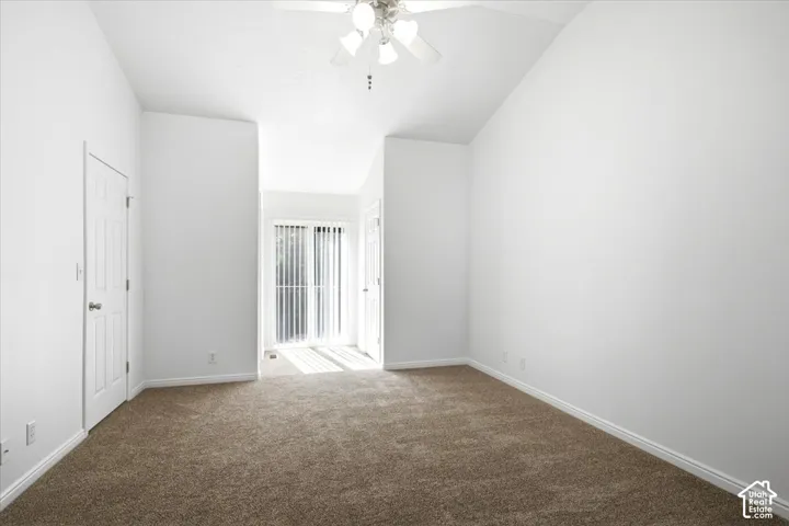 Carpeted room featuring a ceiling fan, vaulted ceiling, white baseboards, and a glass sliding door with vertical blinds