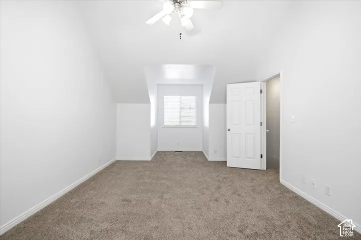 Carpeted room featuring a ceiling fan, sloped ceilings, and a window with blinds