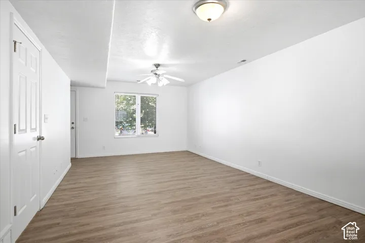 Spacious room featuring wood-finish flooring, white walls, and a ceiling fan with integrated lighting