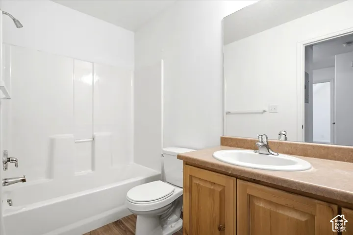 Full bathroom featuring a white tub and shower combination with chrome fixtures, a wood-finish vanity with a built-in sink, a neutral countertop, and wood-finish flooring