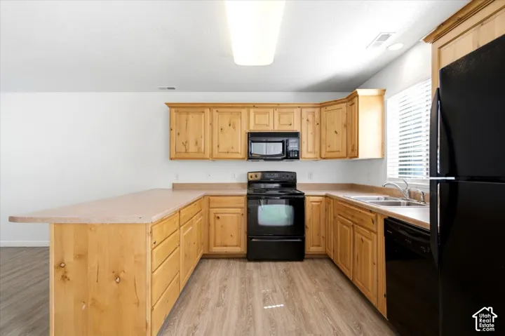 U-shaped kitchen featuring wood cabinetry, laminate countertops, wood-finish flooring, and black appliances