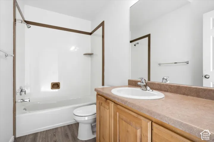 Bathroom featuring a white bathtub and shower combination with a single shelf, wood-finish flooring, light wood vanity with an integrated sink, and a large wall-mounted mirror