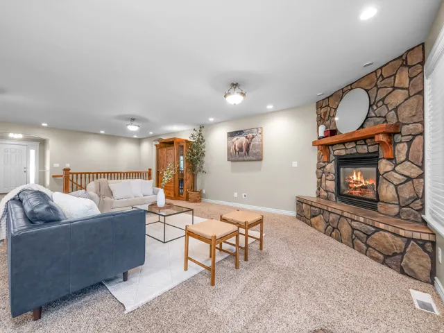 Stone-clad fireplace with a wood mantle and hearth, recessed lighting, carpeted flooring, and a white paneled entry door with sidelights