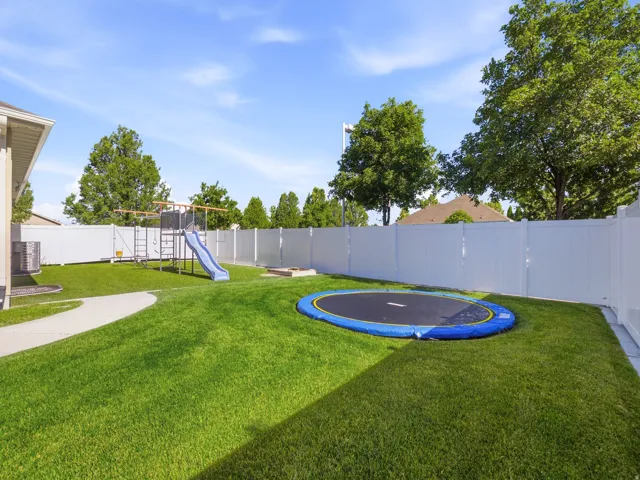 Expansive backyard featuring a lush lawn, white privacy fencing, play area, and a concrete pathway