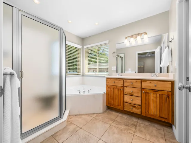 Spacious bathroom featuring a corner soaking tub, a large frosted glass shower enclosure, and an extended vanity with dual sinks