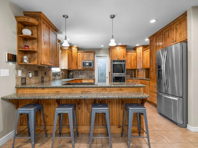 Spacious kitchen featuring extensive wood cabinetry, stone countertops, a breakfast bar with beadboard paneling, built-in stainless steel appliances, and recessed lighting