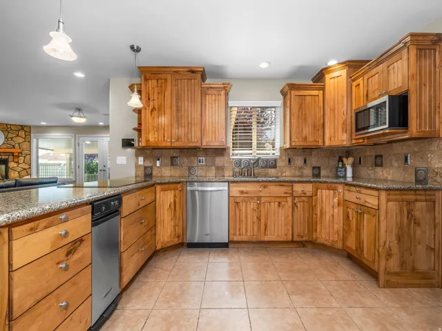 Kitchen featuring wood cabinetry, stainless steel appliances, granite countertops, and tiled flooring