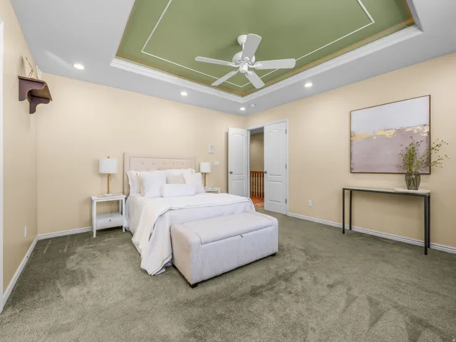 Tray ceiling with green accent paint and recessed lighting in primary bedroom.