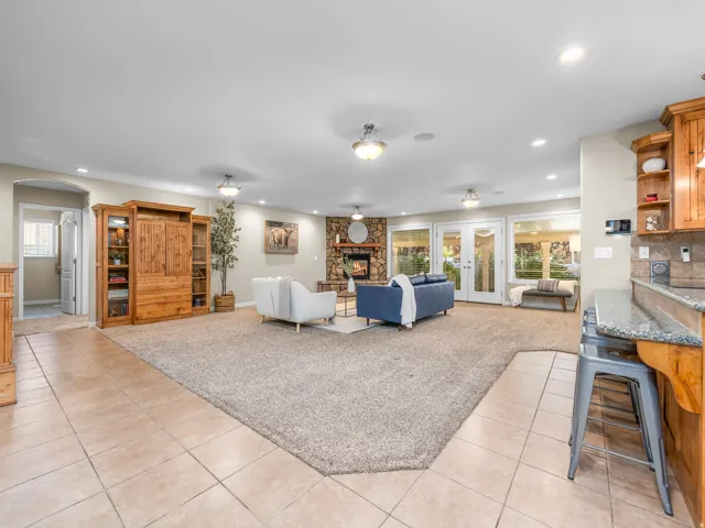 Spacious living area featuring a stone-faced fireplace, multiple French doors, recessed lighting, and a combination of carpet and tile flooring