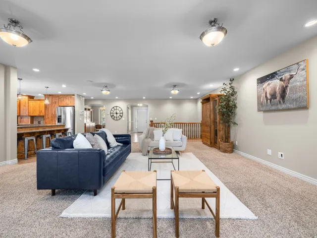 Spacious living area featuring neutral carpeting, recessed lighting, and a partial open concept to a kitchen with wood cabinetry and stainless steel appliances