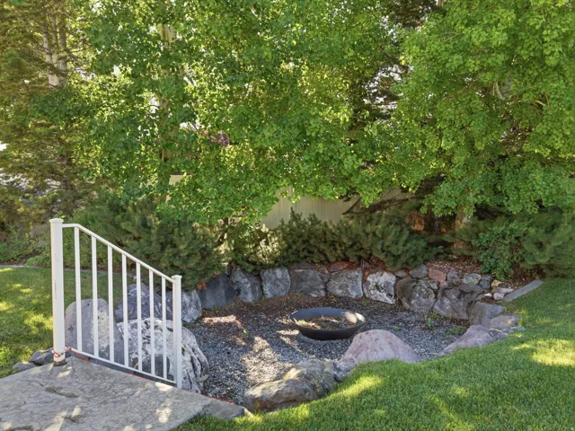 Outdoor fire pit area featuring a gravel base, natural stone retaining wall, and mature foliage surround