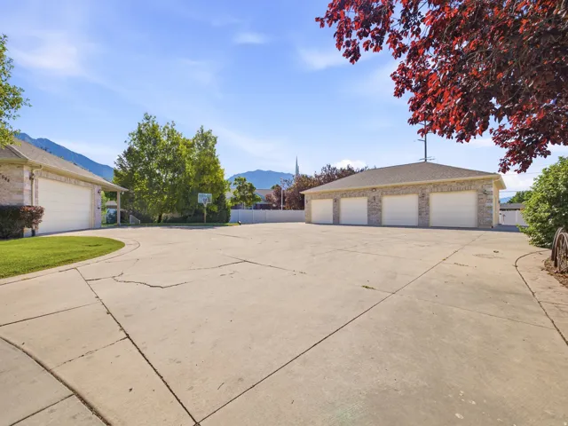 Expansive concrete driveway with a separate structure featuring four garage doors and stone veneer siding