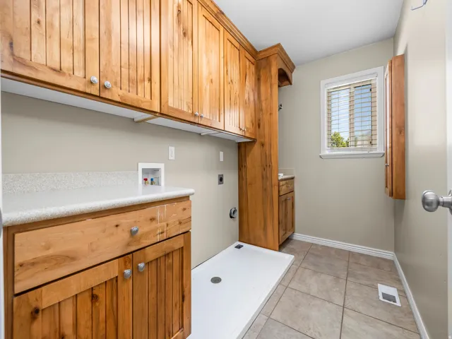 Laundry room featuring wood cabinetry, white countertops, tile flooring, and a window with blinds