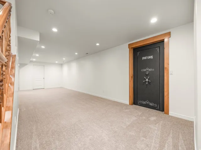 Spacious room featuring a Fort Knox vault door with wood trim, recessed lighting, neutral carpeting, and white walls