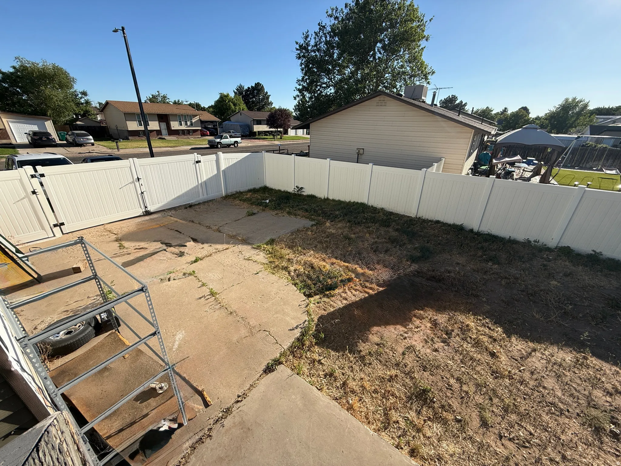 Fenced backyard featuring concrete driveway behind white vinyl privacy fence