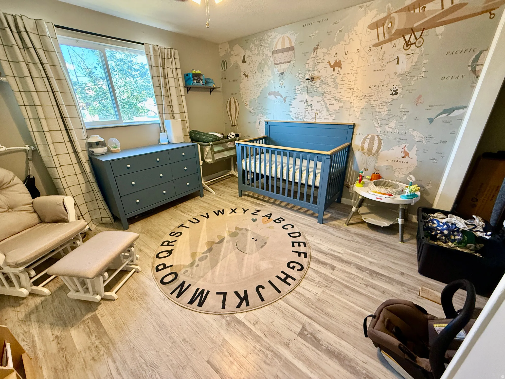 Hardwood-finish flooring featuring a window with natural light, a ceiling fan, and patterned curtains