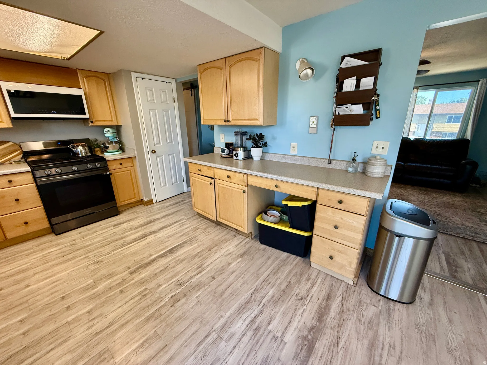 Kitchen featuring wood-finish flooring, light wood cabinetry, a built-in microwave, and a black range