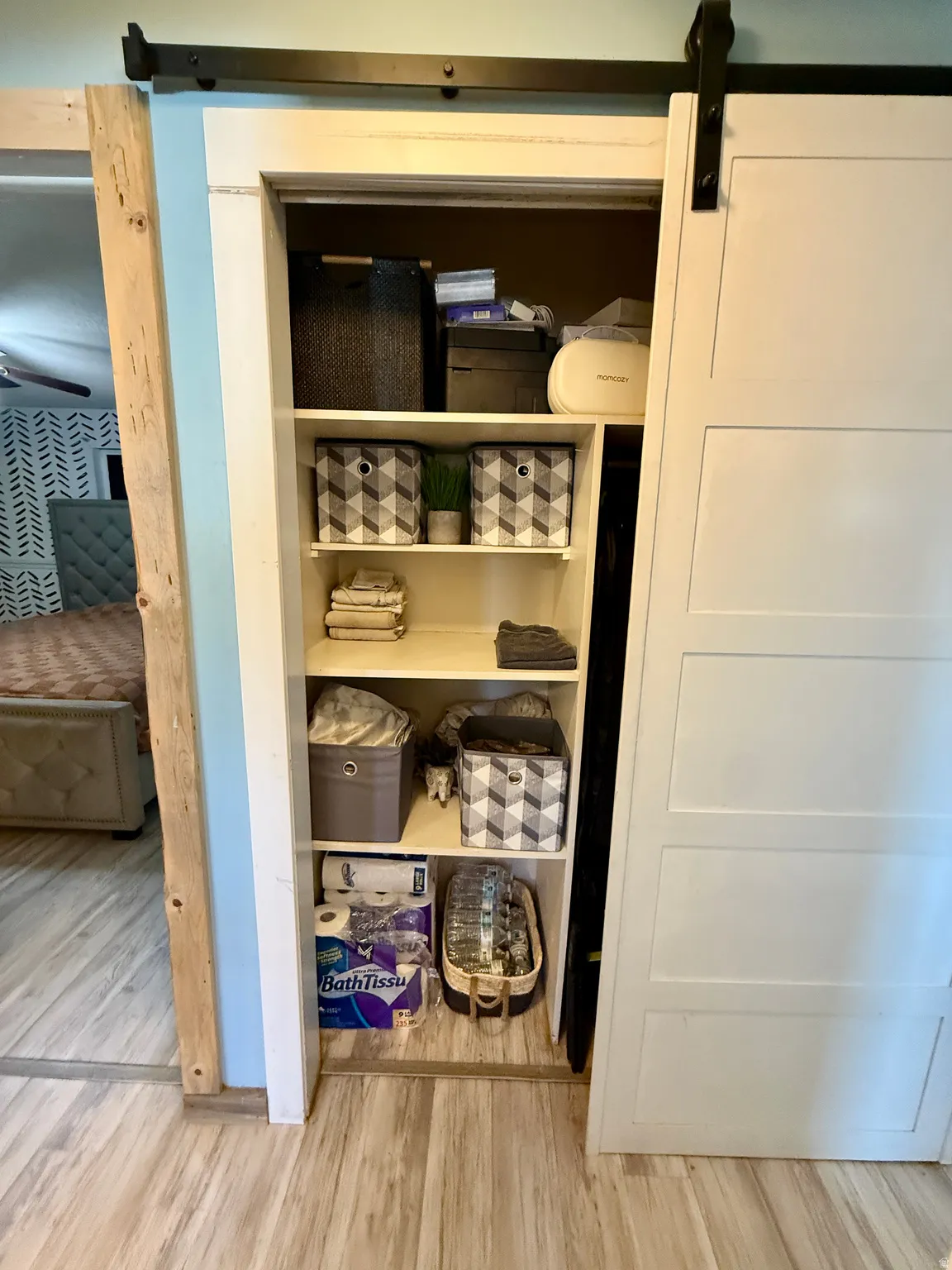 Hall linen closet-Built-in shelving unit with a sliding barn door, wood-finish flooring, and light blue wall paint