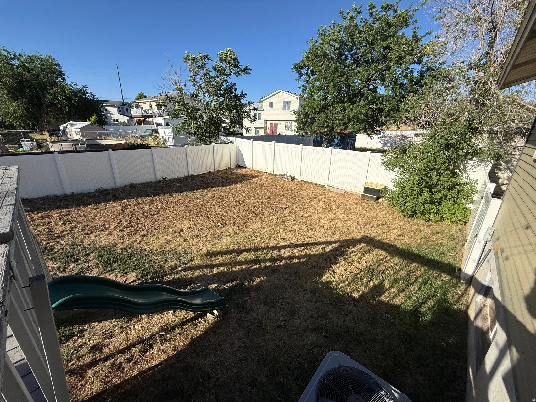 Expansive rear yard featuring a privacy fence, mature trees, and an air conditioning unit