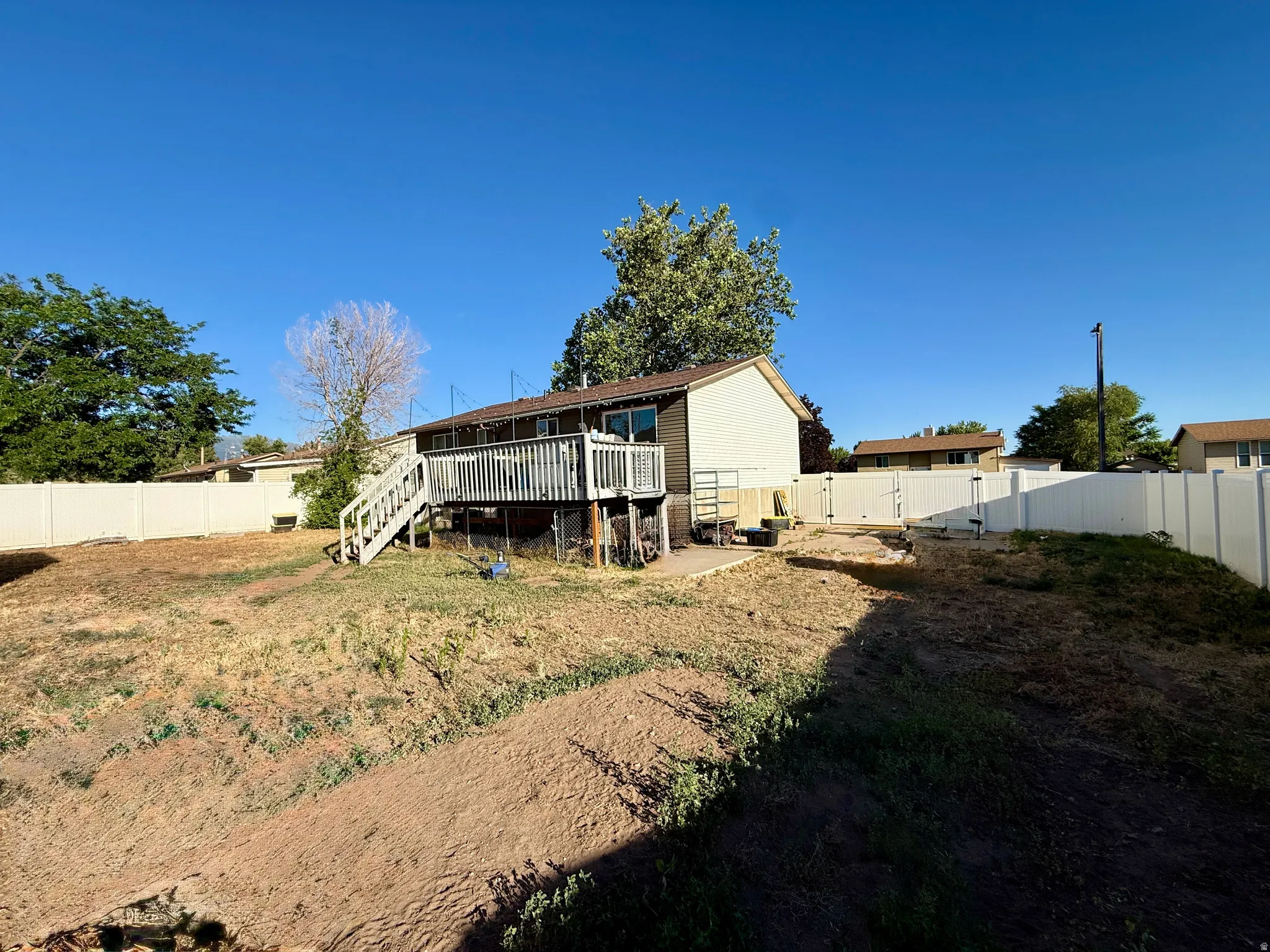 Rear exterior featuring a spacious wooden deck with railings and stairs, a white vinyl privacy fence enclosing the property,