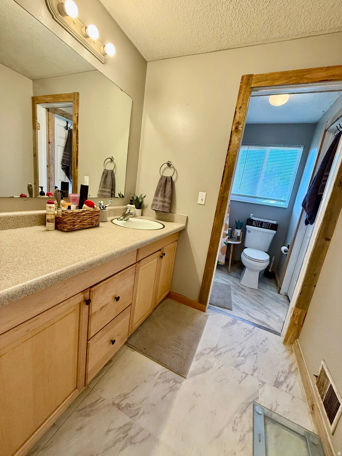 Bathroom featuring a light wood-finish vanity with a built-in sink, an extended countertop, a large wall mirror, and modern overhead lighting, access to master bedroom