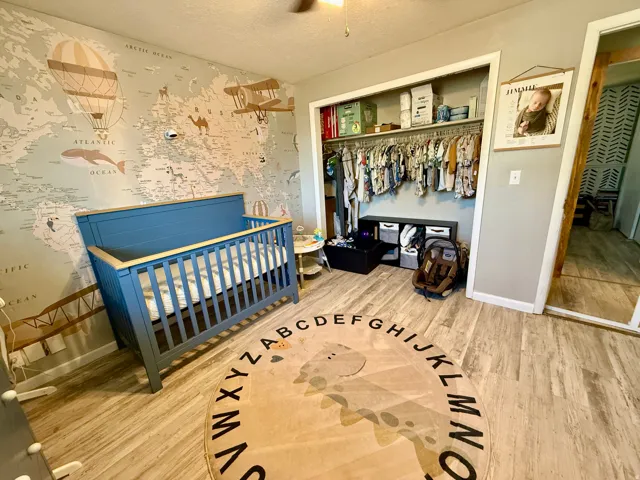 Bedroom featuring wood-finish flooring, a patterned accent wall, and a built-in closet with shelving and hanging storage