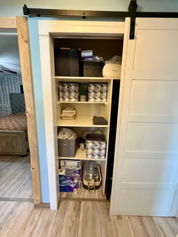 Hall linen closet-Built-in shelving unit with a sliding barn door, wood-finish flooring, and light blue wall paint