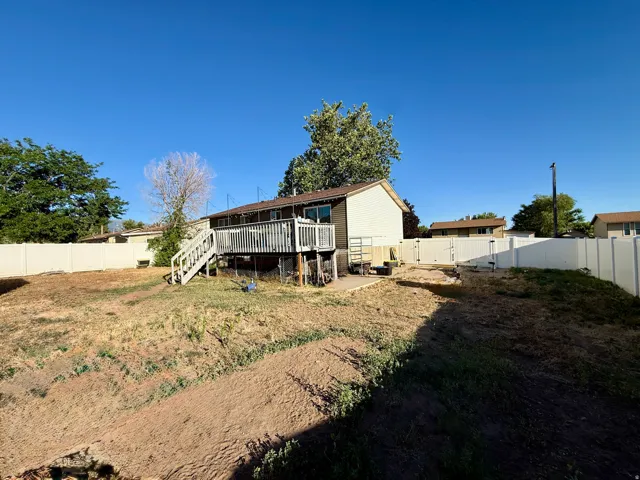 Rear exterior featuring a spacious wooden deck with railings and stairs, a white vinyl privacy fence enclosing the property,