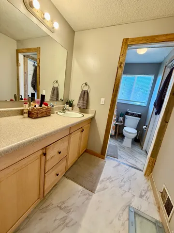 Bathroom featuring a light wood-finish vanity with a built-in sink, an extended countertop, a large wall mirror, and modern overhead lighting, access to master bedroom