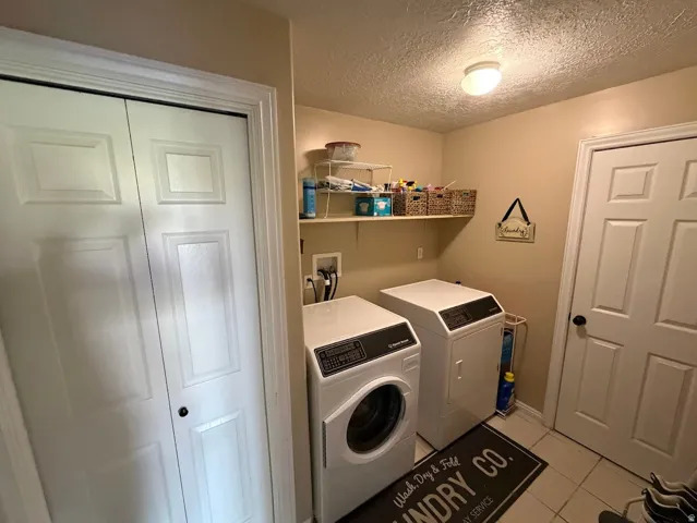 Dedicated laundry area featuring a bi-fold door closet, neutral wall paint, overhead shelving, and tile flooring