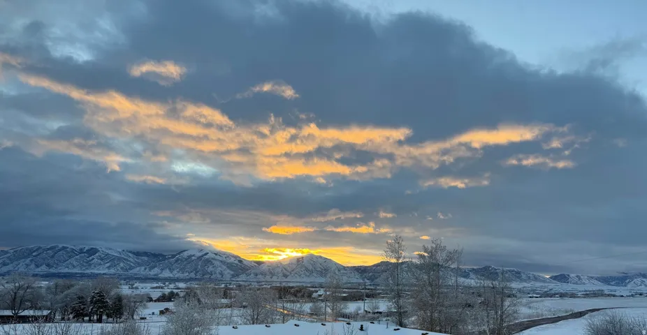 Expansive mountain range backdrop featuring snow-covered peaks and a dramatic sky with golden-hued clouds