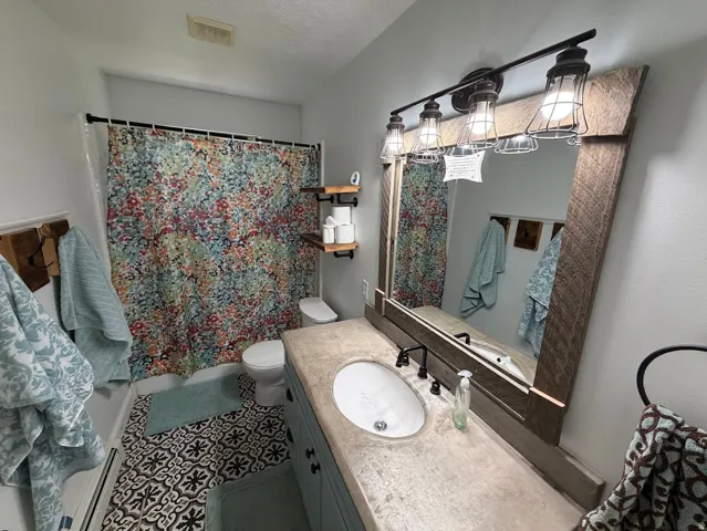 Bathroom featuring patterned floor tiling, a single vanity with an oval sink, and a framed mirror with integrated lighting