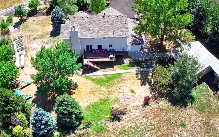 Rear elevation of the residence with a multi-level wood deck, a prominent chimney, and a gravel driveway