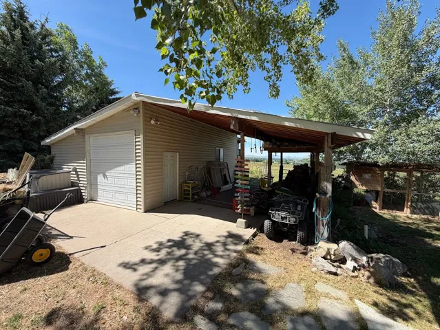Detached garage with horizontal siding, a paneled garage door, and a covered carport with wood-finish supports