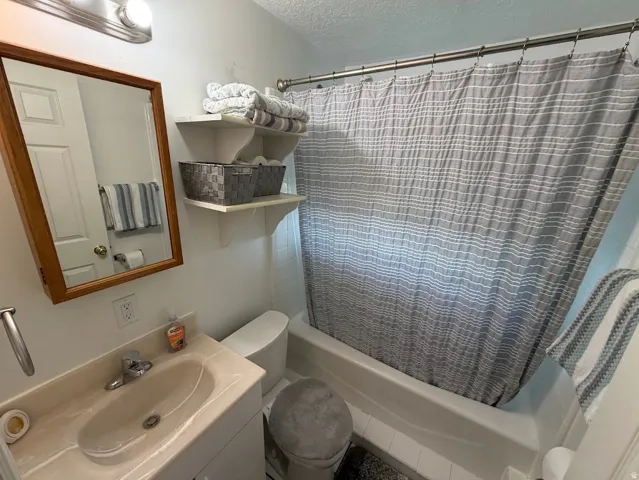 Bathroom featuring a vanity with an integrated sink, a framed mirror, a toilet, and a shower-over-tub combination with a shower rod