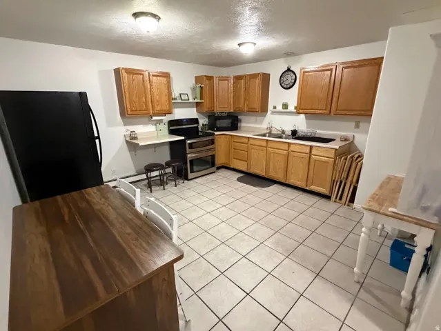 Kitchen featuring wood cabinetry, light-toned countertops, a black refrigerator, and a stainless steel oven