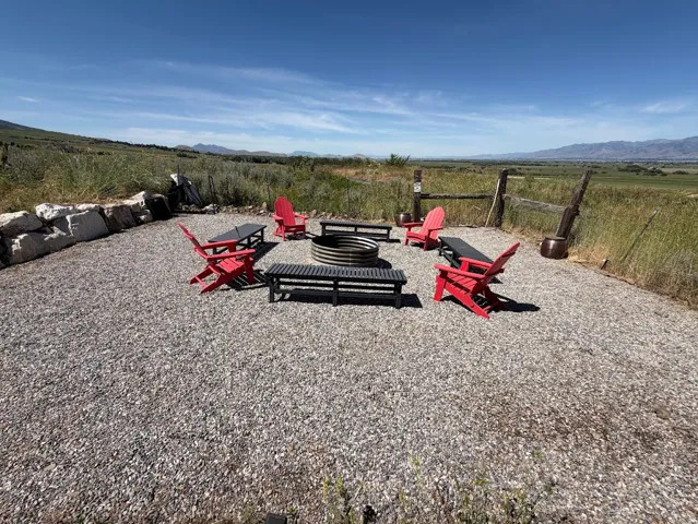 Gravel fire pit area featuring a corrugated metal fire ring, surrounded by a natural wood fence and a stacked stone wall