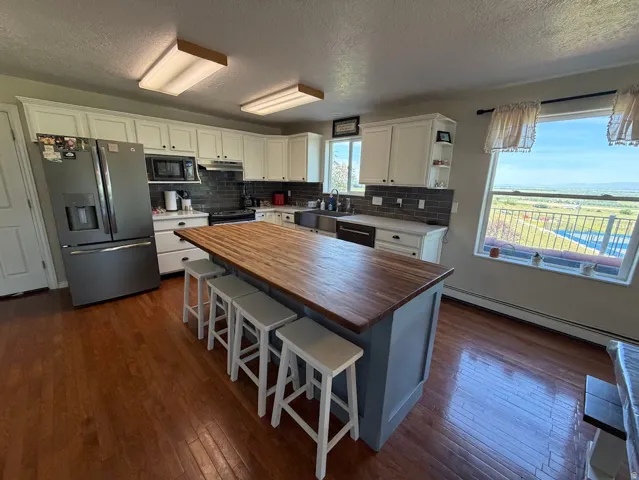 Kitchen featuring a central island with a wood-finish countertop, white cabinetry with dark hardware, a dark subway tile backsplash, and wood-finish flooring